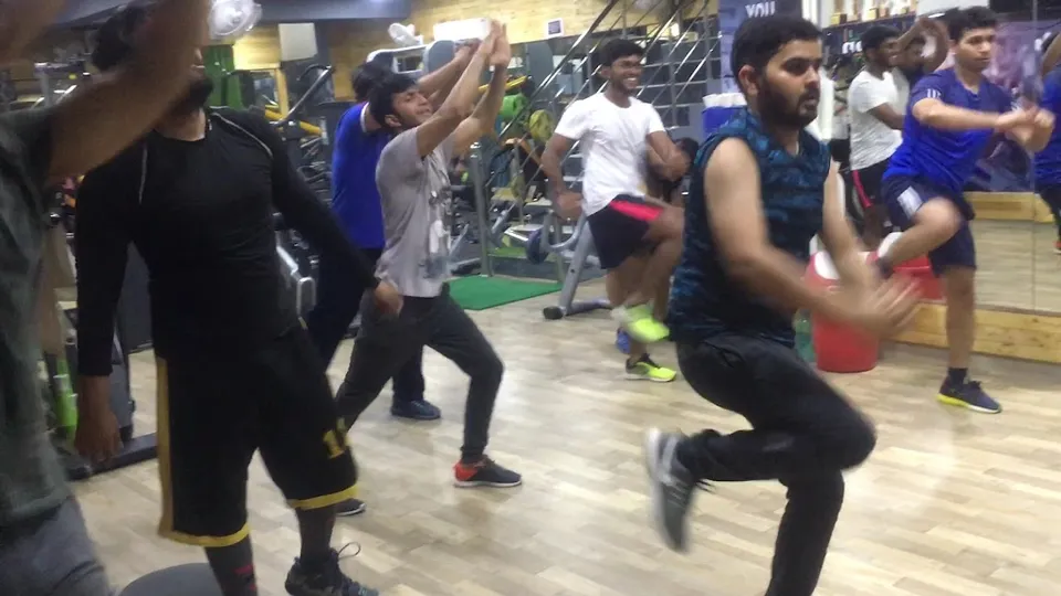 A group of members gathered together at Fitness Factor, with the gym floor and equipment visible around them.